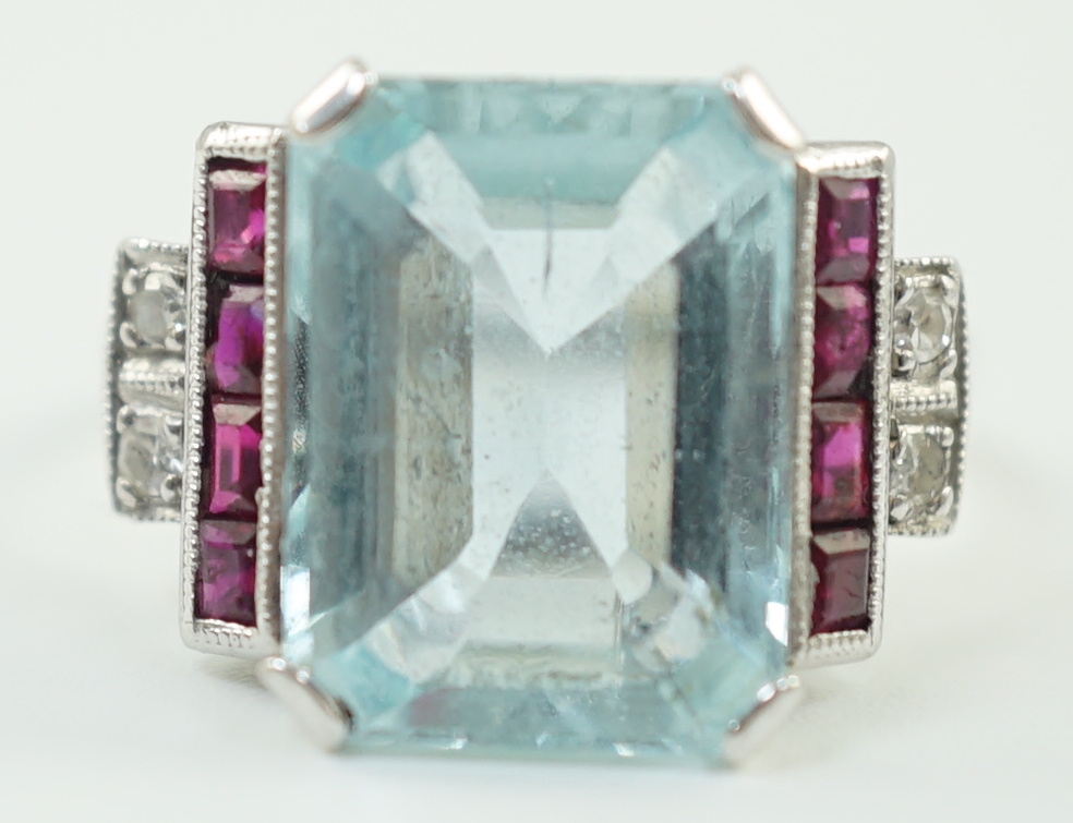 A platinum and single stone emerald cut aquamarine set dress ring, with ruby and diamond set stepped shoulders